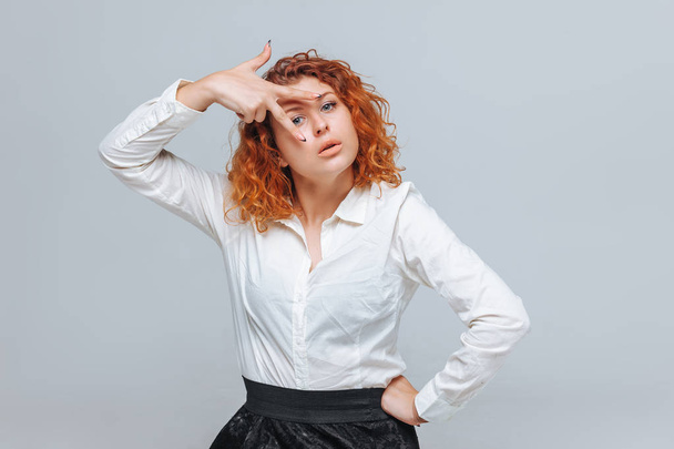 A red-haired girl in a white shirt shows two fingers - Photo, Image