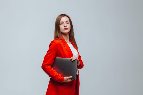 girl in a red jacket holds a laptop on a light background - Zdjęcie, obraz