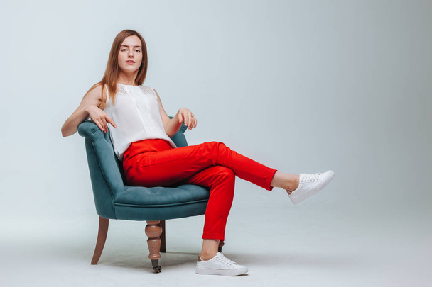 Girl in red pants sitting in a chair on a light gray background - Fotó, kép
