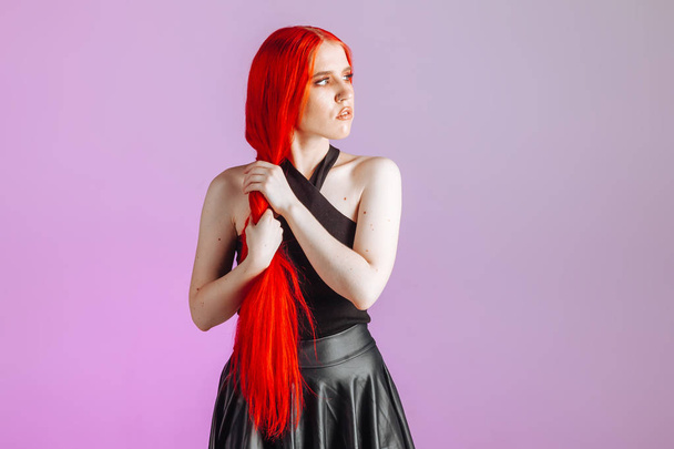 Дівчина з рудим довгим волоссям і шкіряною спідницею позує на рожевому фоні
 - Фото, зображення