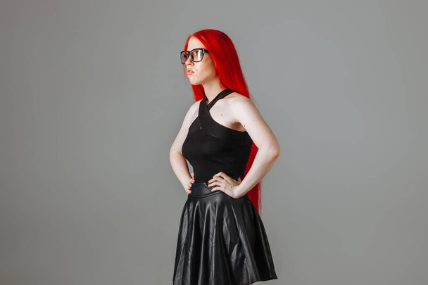 Girl with red long hair wearing glasses and a leather skirt posi - Φωτογραφία, εικόνα