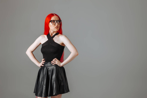 Κορίτσι με κόκκινα μακριά μαλλιά φορώντας γυαλιά και μια δερμάτινη φούστα γωνία μέχρι - Φωτογραφία, εικόνα