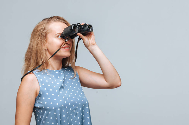 Girl looking through binoculars on a light gray background - Foto, Bild