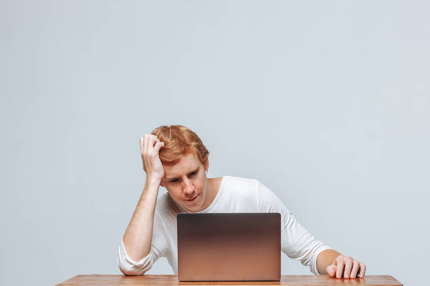 Un hombre piensa para un ordenador portátil en un fondo claro
 - Foto, imagen