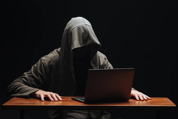 Criminal with laptop in hood on black background - Photo, Image