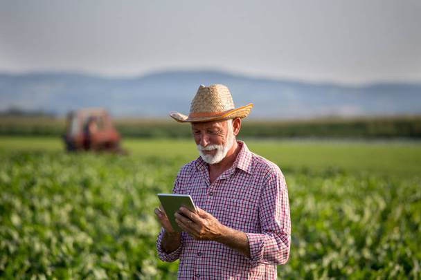 Agricultor con tableta delante del tractor en el campo
 - Foto, Imagen