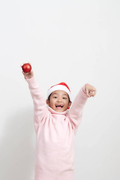 Chica sosteniendo una bola roja de Navidad en suéter y sombrero de santa
 - Foto, imagen