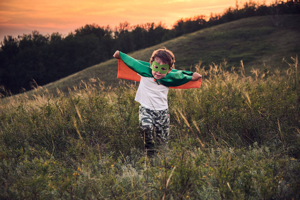スーパーヒーローを演じる小さな男の子。スーパーヒーローの衣装を着た子供幸せな子供は写真家に会うために走る. - 写真・画像