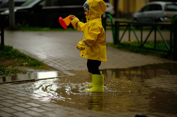 Szczęśliwego dziecka gra w kałuży na letni deszczowy dzień. chłopiec w żółtym płaszczu spacerów w parku. - Zdjęcie, obraz