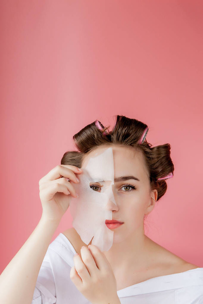 Beautiful young girl with a mask and curlers touching her face. - Fotografie, Obrázek