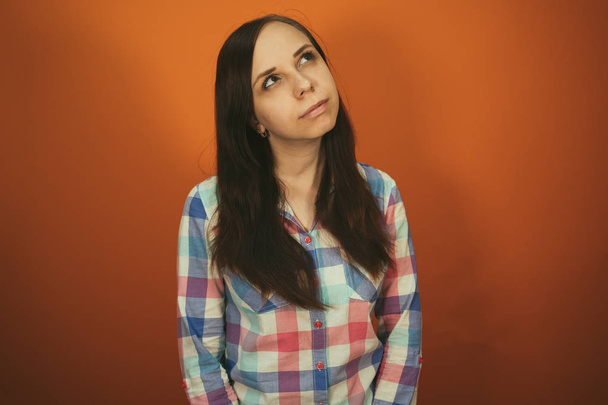 A beautiful woman in a plaid shirt poses on an orange background. - Photo, Image