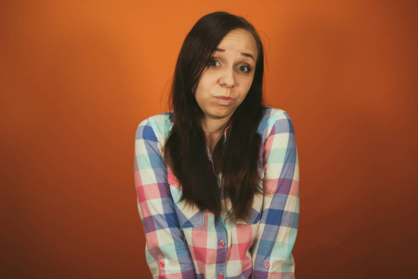 A beautiful woman in a plaid shirt poses on an orange background. - 写真・画像