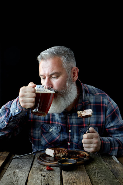 Brutal gray-haired adult man crazy about mustard steak and beer, concept of a holiday, festival, Oktoberfest or St. Patrick's Day - Photo, Image