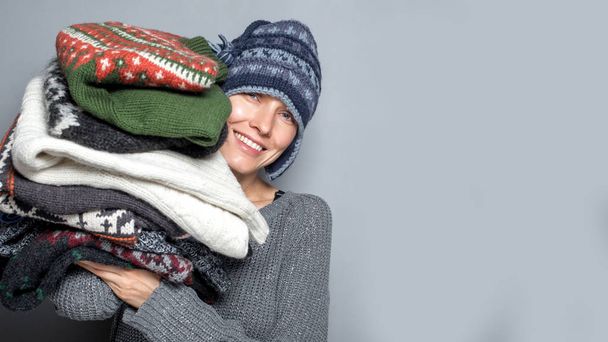 Autumn or winter woman. Portrait of a young woman holding pile of sweaters wearing knitted hat and warm wool sweater - Foto, Imagem