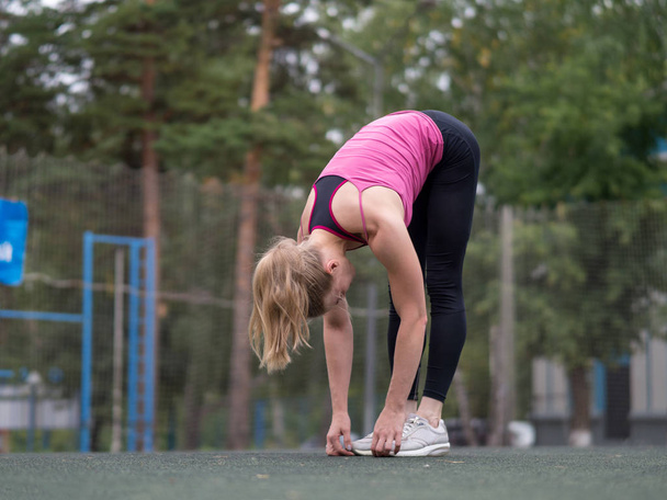 Blond caucasian girl doing warming up before training on the sports ground outdoor, selective focus. - Foto, Bild