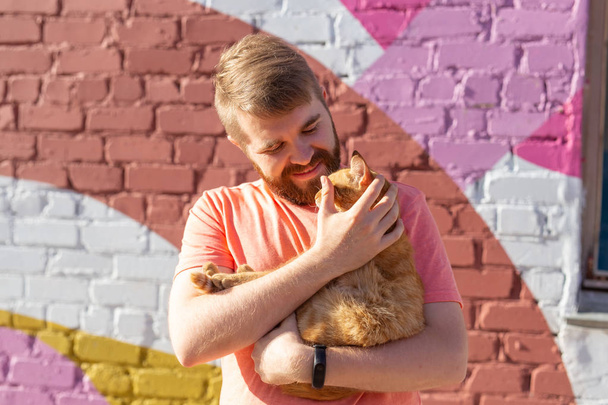 Pet sahibi ve dostluk kavramı - Yakışıklı adam tutuyor ve sevimli zencefil kedi sarılma. Meraklı ifadeile Kedi - Fotoğraf, Görsel
