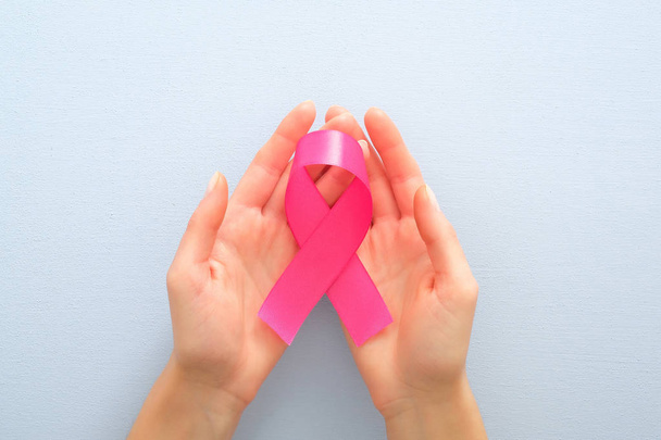 Różowa wstążka świadomości raka piersi w rękach kobiet na niebieskim tle. Koncepcja zdrowia i medycyny kobiet. - Zdjęcie, obraz