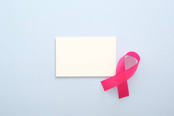 Breast cancer awareness month concept. Empty paper card mockup and pink breast cancer ribbon on blue background. - Foto, Imagen