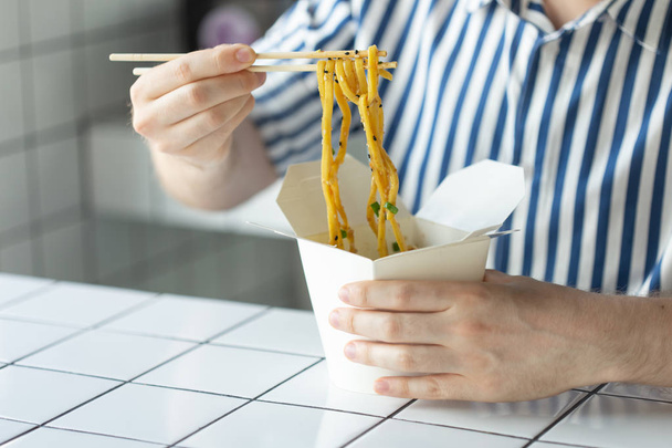 Gros plan d'un jeune homme non identifié main dans une chemise tiennent des bâtons de bois nouilles chinoises. délicieux asiatique cuisine concept
. - Photo, image