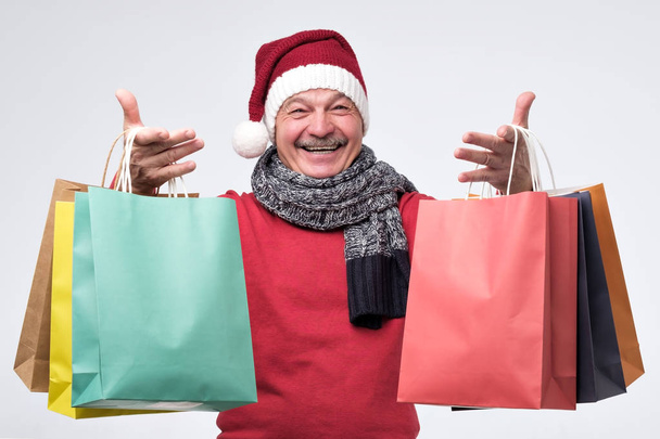 Hombre hispano mayor sosteniendo bolsas de compras de color después de ir de compras
 - Foto, Imagen