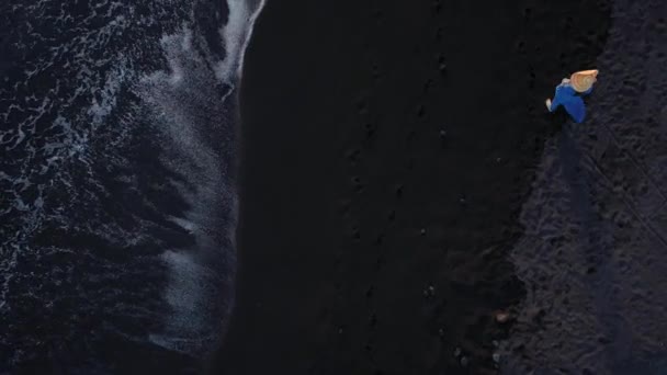 Aerial view of a girl in a blue dress walking on the beach with black sand at sunset. Tenerife, Canary Islands, Spain - Záběry, video