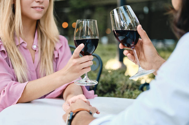 Close up photo of romantic couple with glasses of red wine on date in cafe outdoor - Photo, Image