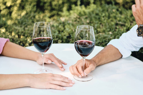 Uzavřete pár sklenicemi červeného vína na romantickém rande v restauraci venkovní - Fotografie, Obrázek