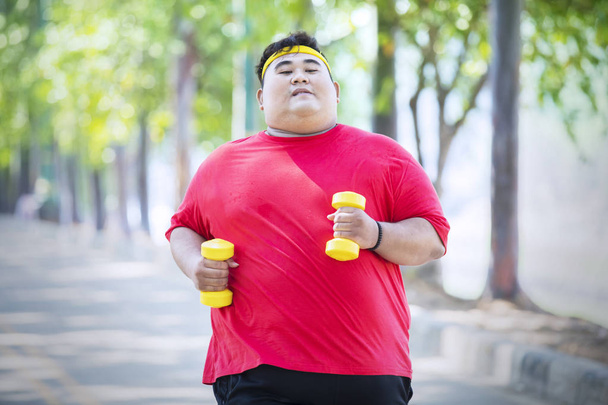 Overweight man runs with dumbbells in the park - Zdjęcie, obraz
