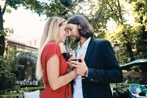 Όμορφο ρομαντικό ζευγάρι με τα ποτήρια του κρασιού ονειρικά αγκάλιασμα στην ημερομηνία στο εστιατόριο υπαίθρια - Φωτογραφία, εικόνα