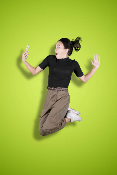 Shocked girl jumping with phone in the studio - Foto, Bild