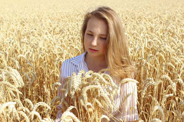 Retrato de una mujer bonita sentada en un campo de trigo de verano y mirando hacia abajo. Personas, naturaleza, libertad y concepto de viaje
. - Foto, Imagen