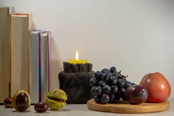Kitaplar, yanan bir mum, kestane, olgun üzüm, elma ve erik beyaz bir arka plan üzerinde Sonbahar natürmort. - Fotoğraf, Görsel