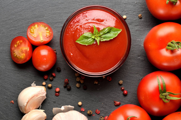 Close-up van Bowl van zelfgemaakte ketchup gemaakt van verse tomaten, knoflook, basilicum op zwarte leisteen plaat. Top View. - Foto, afbeelding