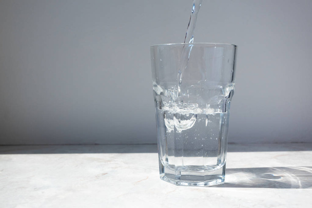 Mineral water pouring into glass on white stone table - Photo, Image