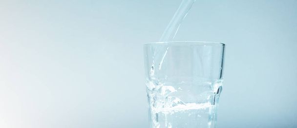 Primer plano de la corriente de vidrio de llenado de agua en un backgro azul pálido
 - Foto, imagen