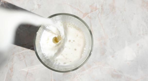 スプラッシュでグラスに注ぐ新鮮な牛乳の流れのトップビュー - 写真・画像