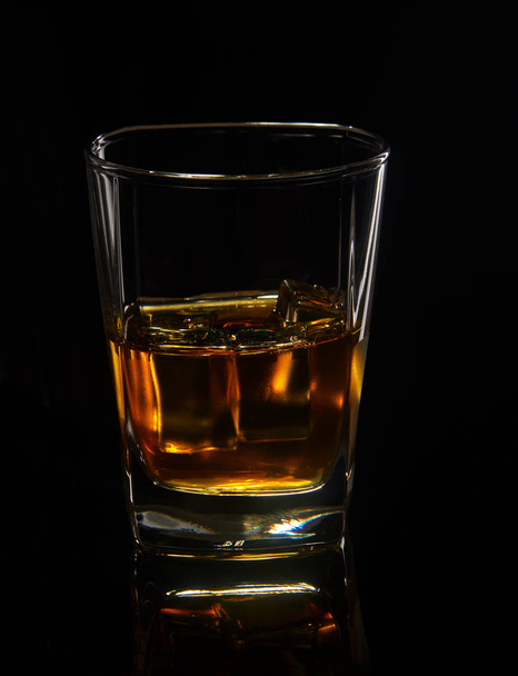 Glass of whiskey with ice on a black background with reflection - Zdjęcie, obraz