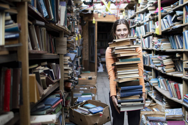 meisje student draagt een grote stapel boeken in de bibliotheek, voorbereiding voor studie, kennis is macht, concept - Foto, afbeelding