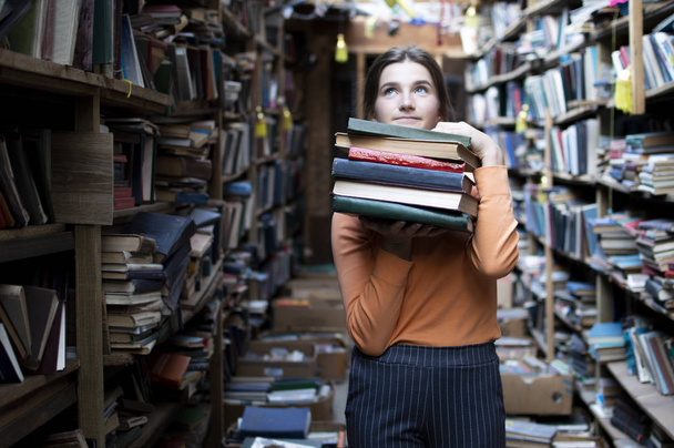 girl student holds a stack of books in the library, she searches for literature and offers to read, a woman prepares for study, knowledge is power, concept bookseller - Fotografie, Obrázek