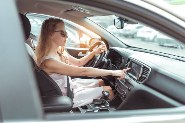 A woman in car, selects navigation application on touch screen display. pink dress. automatic gearbox, in parking lot near shopping center, car interior, radio station selection. - Photo, Image