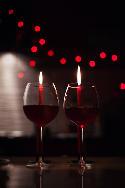 Jantar romântico: dois copos de vinho e velas estão no escuro com luzes de ano novo no fundo
 - Foto, Imagem