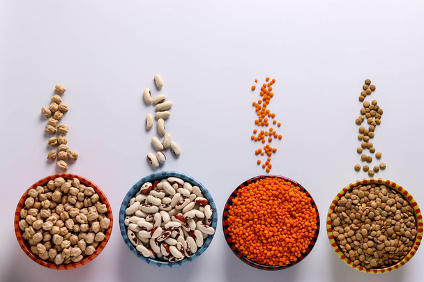 Красная и коричневая чечевица, горох и белая фасоль являются бобовыми, которые содержат много белка расположены на белом фоне в мисках, горизонтальной ориентации
 - Фото, изображение