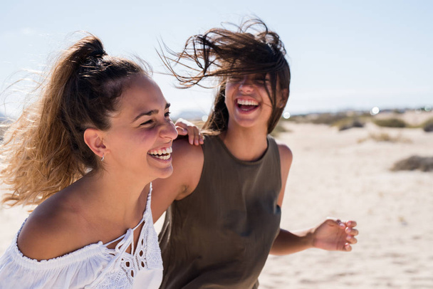 The wind is blowing the young girls hair as they walk along the beach and laugh - Photo, image