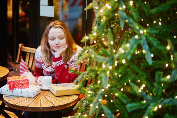 Girl in holiday sweater drinking coffee or hot chocolate in cafe decorated for Christmas - Fotografie, Obrázek