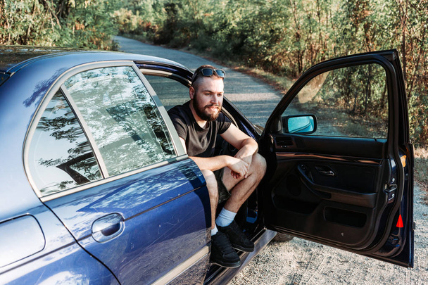 Bearded man sitting in the front of the car, open door, waiting for someone. - Photo, Image