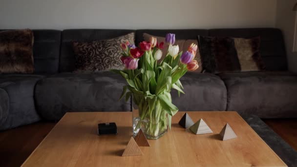 Wazon z wielkim bukietem kolorowych tulipany na drewnianym stole w nowoczesnym salonie - Materiał filmowy, wideo