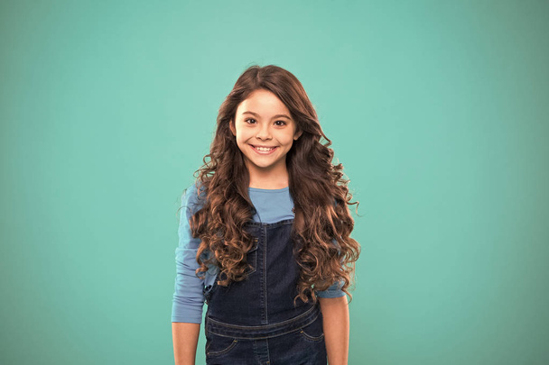 Extreme hair volume. Kid girl long healthy shiny hair. Kid happy cute face with adorable curly hairstyle stand over blue background. Little girl grow long hair. Teaching healthy hair care habits - Zdjęcie, obraz