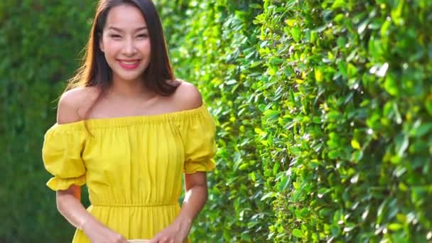 zdjęcia pięknej Azjatki w żółtej sukience przed zielonym krzakiem - Materiał filmowy, wideo