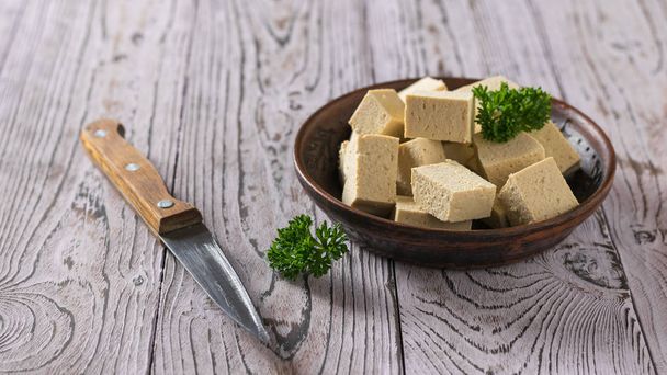 Kil kasede tofu peyniri parçaları ve tahta bir masada bıçak. Soya peyniri. - Fotoğraf, Görsel