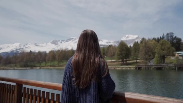 Long-hair brunette woman standing and looking scenic view of mountain lake in Switzerland. Rear view. Focus on female hair - Footage, Video